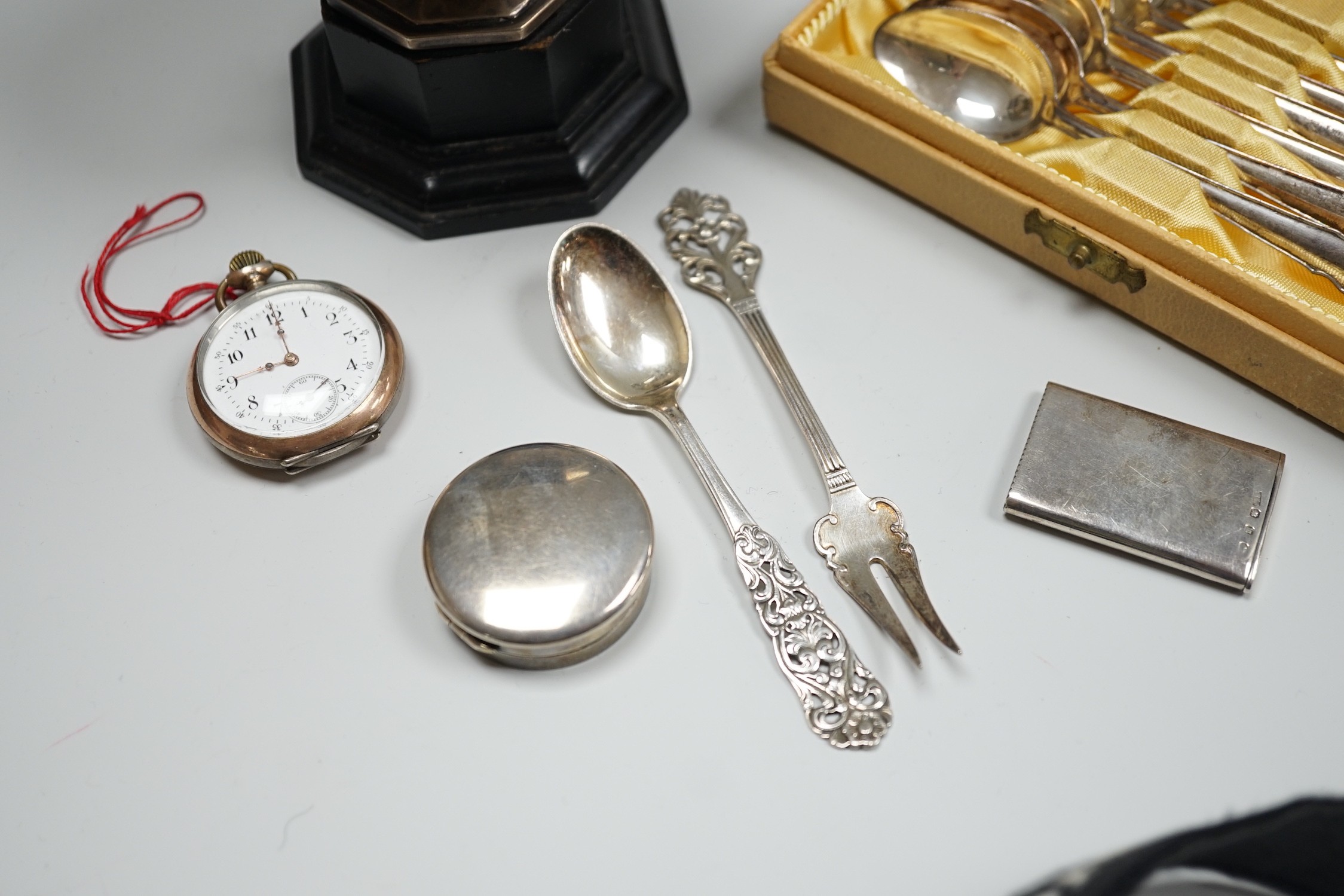 A late Victorian silver vesta case, a silver pill box, a small silver trophy cup, a cased set of six Swedish white metal coffee spoons, a similar spoon and fork and an early 20th century tow colour white metal fob watch.